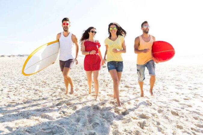 Un groupe d'amis souriants se promène sur le sable, tout excités à l'idée d'aller à la plage pour surfer.