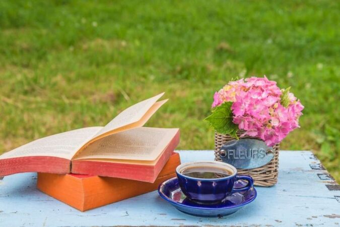Un livre ouvert et une tasse de café sur une table en bois lors d'une pause bien-être en extérieur.