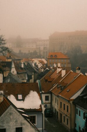 Une vue de toits de tuiles oranges d'une ville historique européenne sous un ciel de brume matinale, illustrant les avantages de voyager hors saison en europe.